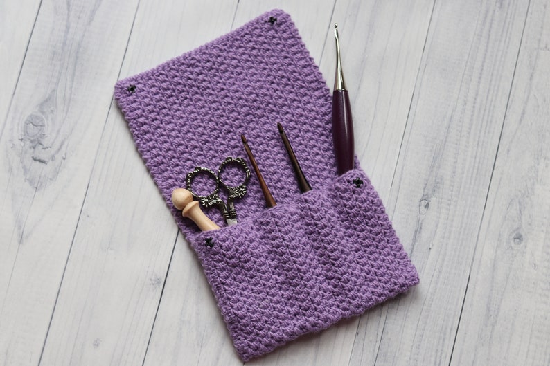 May include: A purple crocheted pouch with a flap, containing a pair of scissors, a wooden dowel, and three crochet hooks.