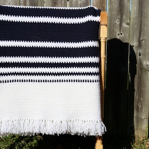 May include: A white and navy blue striped crocheted throw blanket with white fringe. The blanket is draped over a wooden chair.