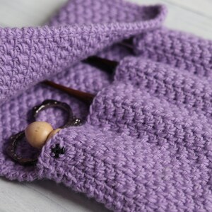 May include: Purple crocheted pouch with a wooden bead and metal rings inside. The pouch has a flap that closes with a button.