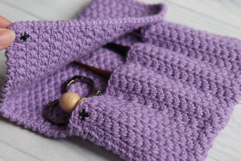 May include: Purple crocheted pouch with a wooden bead and metal rings inside. The pouch has a flap that closes with a button.