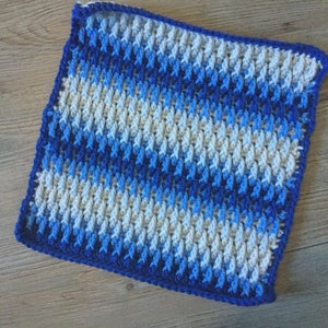 Peut inclure: Un carré crocheté bleu et blanc avec un motif texturé. Le carré a une bordure bleue.