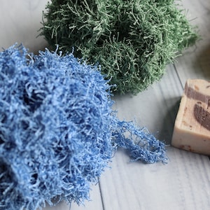 May include: Four bath poufs in different colors: blue, green, yellow, and brown. The poufs are made of a soft, fluffy material. A bar of soap with the text "Freshis" is also visible.