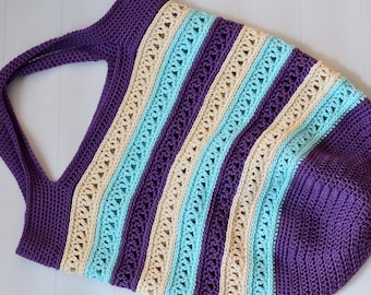 May include: A crocheted tote bag with purple, cream, and light blue stripes. The bag has a wide, open top and a single handle.