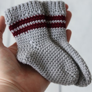 Puede incluir: Un par de calcetines de punto grises con dos rayas burdeos alrededor de la parte superior de cada calcetín.