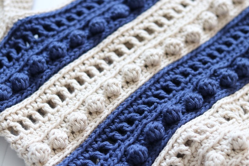 May include: Close-up of a crocheted fabric with alternating stripes of beige and navy blue. The fabric has a textured, bumpy surface with small, round, crocheted balls.