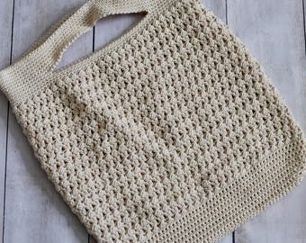 May include: A cream-colored, crocheted tote bag with a single handle. The bag features a textured stitch pattern and a rectangular shape. The handle is wide and integrated into the bag's design. The bag is made of a soft, natural fiber.