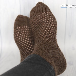 May include: Brown crocheted socks with a lacy pattern. The socks are worn on a person's feet.