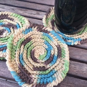 May include: Three crocheted coasters in shades of brown, green, and blue. The coasters are in a swirl pattern and are arranged in a circle.
