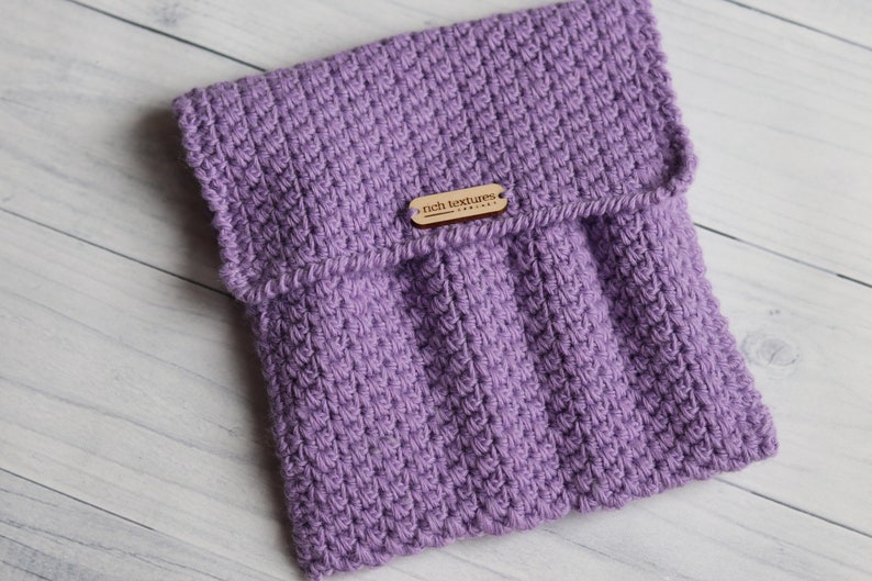 May include: A purple knitted pouch with a flap closure and a wooden tag that reads "rich textures".