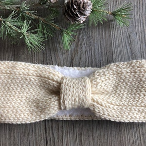 May include: A cream-colored knitted headband with a bow detail. The headband is made of a soft, cozy yarn and is perfect for keeping your ears warm in the winter.