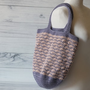 May include: A crocheted tote bag with a wavy pattern in shades of purple and pink. The bag has a single strap and is made with a textured yarn.