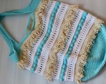 May include: A crocheted tote bag with a light blue, white, and beige striped pattern. The bag has fringe trim and a crocheted handle.