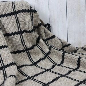 May include: A beige and black crocheted throw blanket with a checkered pattern.