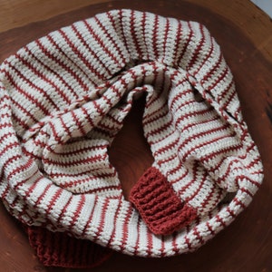 May include: A white and red striped crocheted infinity scarf with red crocheted ends.