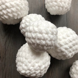 May include: A group of six white crocheted balls, resembling snowballs, are arranged on a wooden surface.