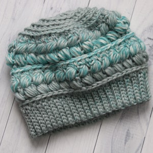 May include: A crocheted beanie hat in shades of teal and gray with a textured, bobbly design.