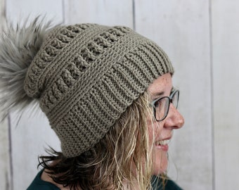 May include: A brown crocheted beanie with a faux fur pom pom. The beanie has a textured stitch pattern.