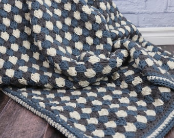 Pode incluir: Uma manta de crochê com um padrão xadrez em tons de azul e branco. A manta é feita com um ponto texturizado que lhe confere um aspeto fofo.
