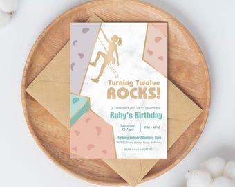 May include: A pink, blue, and purple birthday invitation with a gold silhouette of a person rock climbing. The invitation reads "Turning Twelve ROCKS!" and includes the text "Come and join us to celebrate Ruby's Birthday" and details for the event.