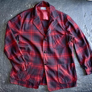 May include: A long-sleeve button-up jacket featuring a red and black plaid pattern. The jacket includes a notched lapel, one chest pocket, two lower front pockets, and dark buttons. The interior is lined with a solid red fabric and a small label.