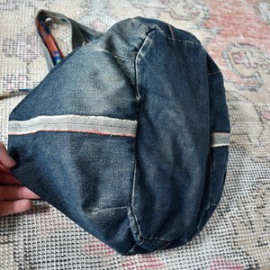 Puede incluir: Un bolso tote de mezclilla azul con rayas blancas y rojas. El bolso tiene forma redondeada y un asa de tela estampada. El bolso est&aacute; sobre una alfombra estampada.