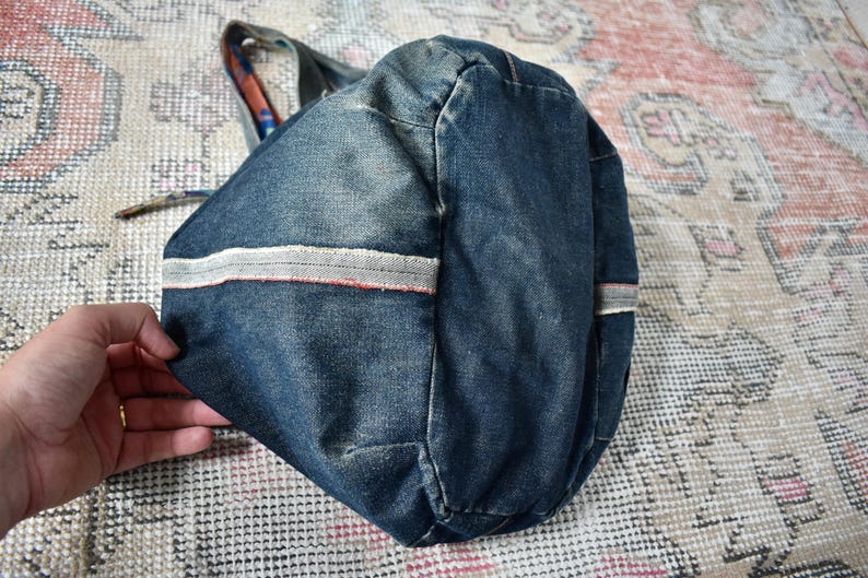 Puede incluir: Un bolso tote de mezclilla azul con rayas blancas y rojas. El bolso tiene forma redondeada y un asa de tela estampada. El bolso est&aacute; sobre una alfombra estampada.