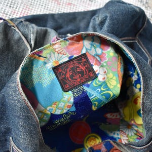Puede incluir: Un bolso tote de mezclilla con un interior estampado floral colorido. El interior del bolso presenta una vibrante mezcla de dise&ntilde;os florales azules, verdes y amarillos. Una etiqueta negra con texto rojo es visible dentro del bolso.