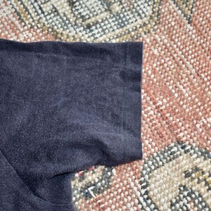 May include: A short-sleeved t-shirt in a solid dark charcoal gray color. The garment features a standard crew neck construction with visible stitching along the sleeve hem and shoulder seam, showcasing a plain and simple textile design.