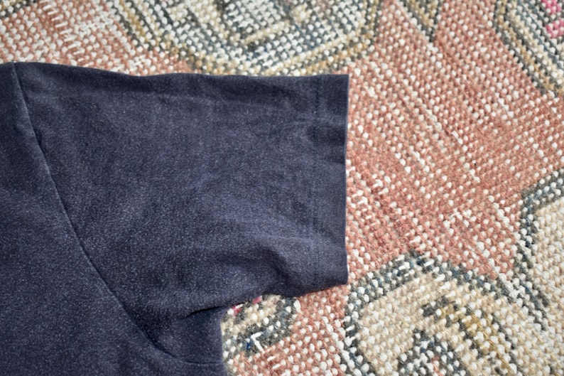 May include: A short-sleeved t-shirt in a solid dark charcoal gray color. The garment features a standard crew neck construction with visible stitching along the sleeve hem and shoulder seam, showcasing a plain and simple textile design.