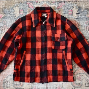 Könnte beinhalten: Vintage rot-schwarz karierte Jacke mit Reißverschluss, Kragen und einer Brusttasche. Die Jacke hat zwei Seitentaschen und ist aus einem dicken, warmen Material gefertigt.