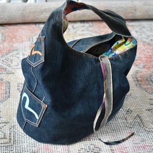 Puede incluir: Bolso hobo de mezclilla azul oscuro con una sola correa para el hombro. El bolso presenta dos peque&ntilde;os bolsillos de mezclilla con dise&ntilde;os coloridos. El forro interior es un vibrante estampado floral. Un accesorio elegante y pr&aacute;ctico.