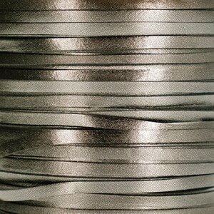 May include: Close-up of a spool of silver and black metallic ribbon. The ribbon is wound tightly and has a shiny, reflective surface.