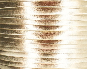 May include: Close-up of a roll of gold leather cord. The cord is made of thin strips of leather that are woven together. The leather has a shiny, metallic finish.