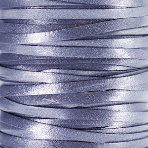 Op de afbeelding: Close-up van een spoel met zilverkleurige leren koord. Het koord is gemaakt van dunne stroken leer die met elkaar zijn verweven.