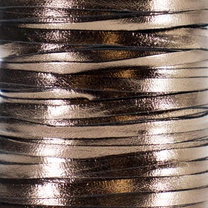 May include: Close-up of a spool of metallic gold leather cord. The cord is flat and thin, with a shiny, reflective surface. The cord is tightly wound, creating a textured, layered effect. The overall color is a warm gold with dark undertones.