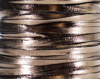 May include: Close-up of a spool of metallic gold leather cord. The cord is flat and thin, with a shiny, reflective surface. The cord is tightly wound, creating a textured, layered effect. The overall color is a warm gold with dark undertones.