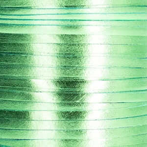 May include: Close-up of a stack of light green leather strips. The strips are arranged in a horizontal pattern, creating a textured and shiny surface.