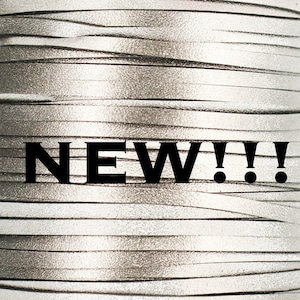 May include: A close-up of a silver leather cord with the word "NEW!!!" printed on it.