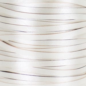 May include: Close-up of a spool of off-white leather strips. The strips are layered and curved, creating a textured, woven appearance. The leather has a subtle sheen, and the edges show a hint of a darker tone.