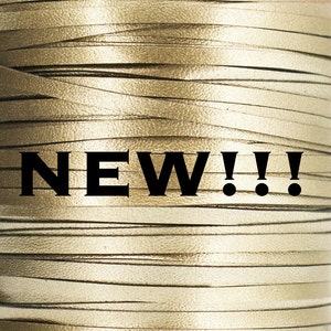 May include: A close-up of a spool of gold leather cord. The cord is made of thin strips of leather that are woven together. The text "NEW!!" is printed on the spool.