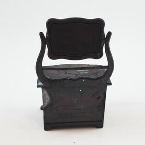 May include: Black metal pencil sharpener shaped like a vanity with a mirror. The sharpener has a drawer and a small shelf. The text "MADE IN JAPAN" is visible on the bottom.
