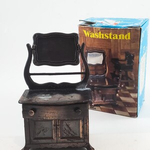 May include: A vintage metal pencil sharpener shaped like a washstand with a mirror and a drawer. The sharpener is brown and has a woodgrain finish. The box says "Washstand" on it.