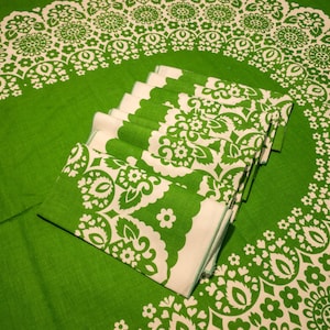 May include: A set of green and white patterned napkins folded and stacked on a green tablecloth with a matching pattern. The napkins have a white background with a green floral design.