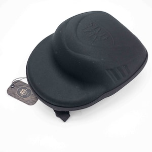 Op de afbeelding: Zwarte harde beschermhoes voor een hoed met de tekst "The Hat Life" in reliëf op de bovenkant. De hoes heeft een band en een klein label met de tekst "The Hat Life" en een logo.