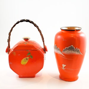 May include: A set of two orange ceramic vases with a hand-painted design. The smaller vase has a lid and a woven handle. The larger vase has a mountain scene with a boat.