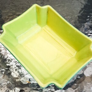 May include: A green and yellow ceramic baking dish with a rectangular shape. The dish has a glazed finish and is designed for baking.