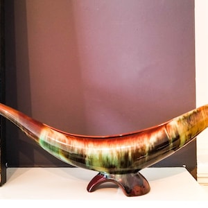 May include: A large, ceramic, horn-shaped bowl with a brown, green, and white glaze. The bowl is sitting on a white surface.