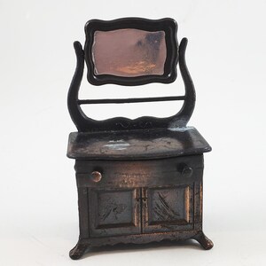 May include: A vintage metal pencil sharpener shaped like a vanity with a mirror and a drawer. The sharpener is painted in a dark brown colour and has a distressed finish.