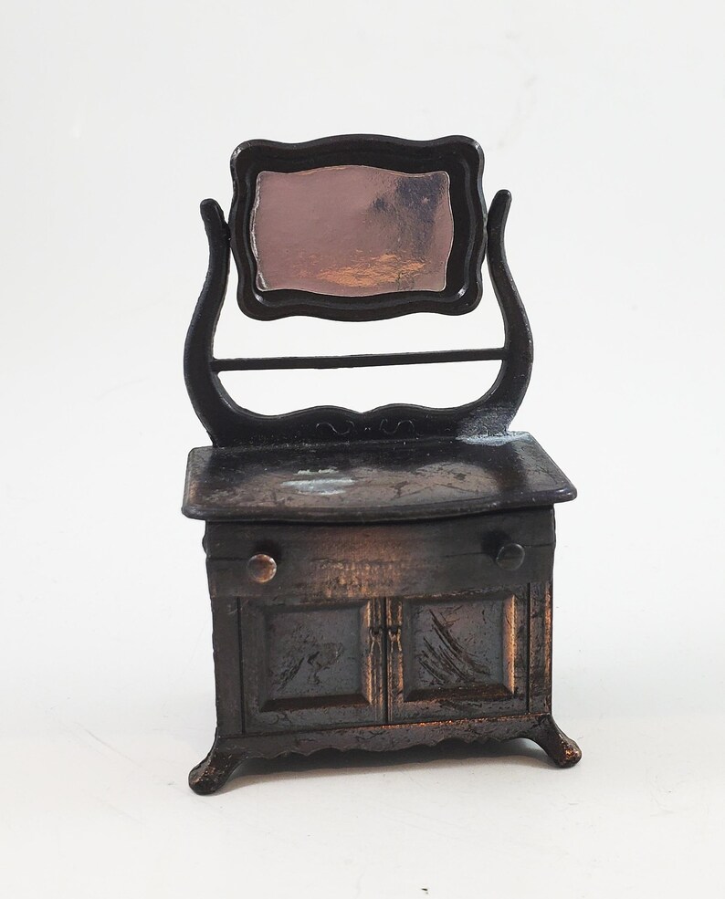 May include: A vintage metal pencil sharpener shaped like a vanity with a mirror and a drawer. The sharpener is painted in a dark brown colour and has a distressed finish.