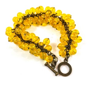 May include: A yellow beaded bracelet with a brass clasp. The bracelet is made of many small, round beads that are strung together on a wire.